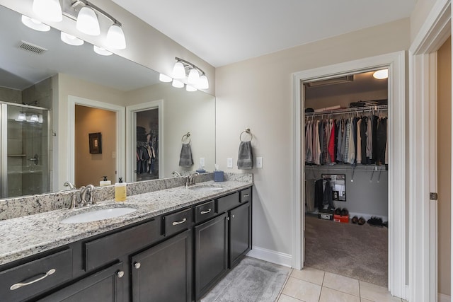 full bathroom with double vanity, a sink, a shower stall, a spacious closet, and tile patterned floors