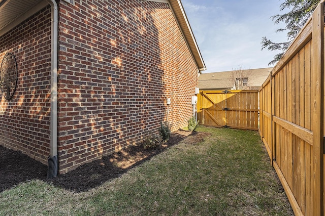 view of side of home featuring brick siding, a gate, fence, and a lawn