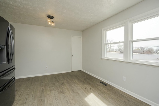 unfurnished dining area with visible vents, a textured ceiling, baseboards, and wood finished floors