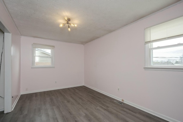 empty room featuring a healthy amount of sunlight, a textured ceiling, visible vents, and dark wood-style flooring