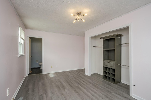 unfurnished bedroom with baseboards, wood finished floors, ensuite bathroom, a textured ceiling, and a closet