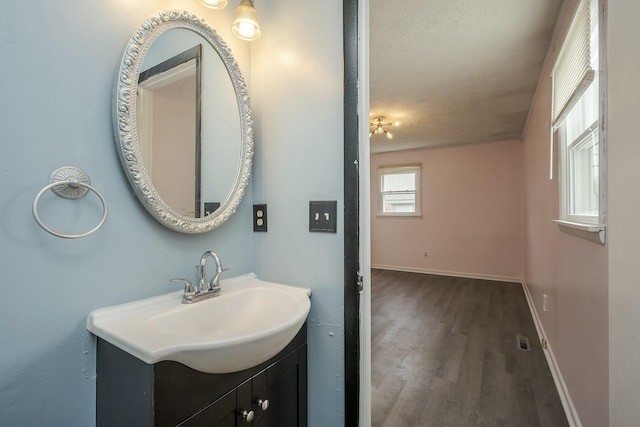 bathroom with a textured ceiling, baseboards, wood finished floors, and vanity