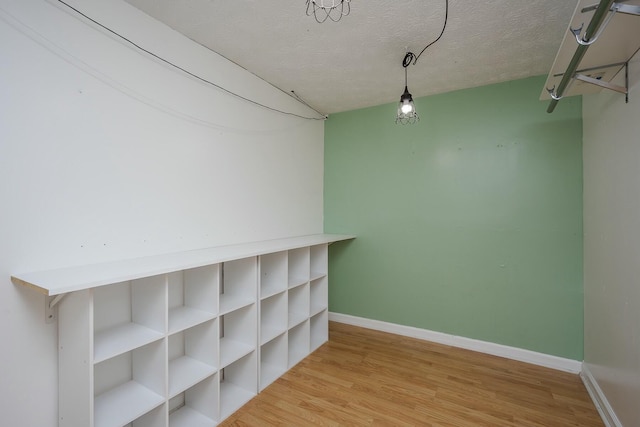 interior space featuring light wood-type flooring, a textured ceiling, and baseboards