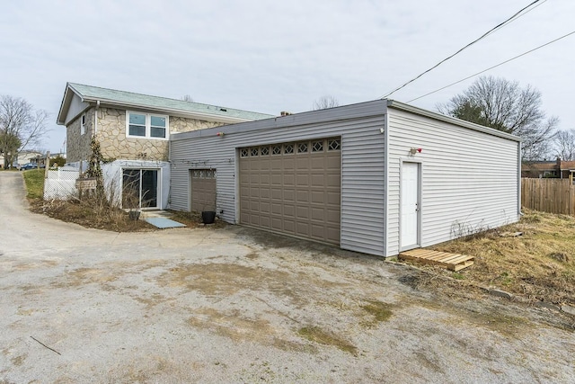 exterior space with a garage, stone siding, fence, and an outbuilding