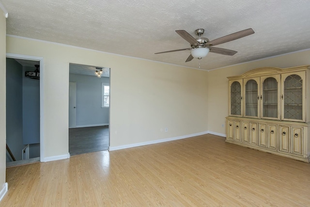 spare room featuring light wood-type flooring, crown molding, a textured ceiling, and baseboards