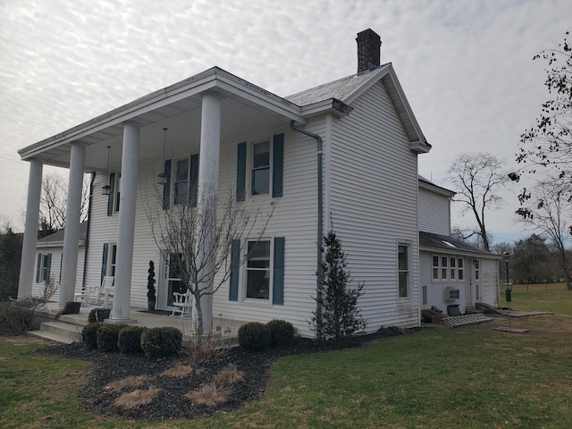 view of side of home with a porch, a lawn, and a chimney