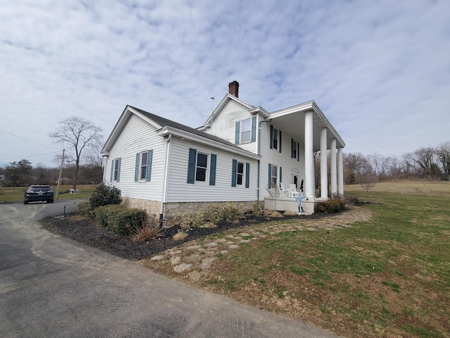 view of side of home featuring covered porch, a chimney, and a lawn