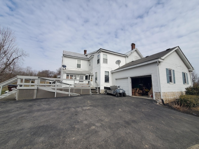 view of front facade with an attached garage, a chimney, aphalt driveway, and a wooden deck