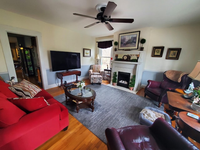 living room with a brick fireplace, ceiling fan, baseboards, and wood finished floors