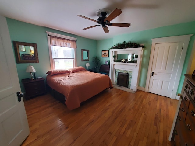 bedroom with ceiling fan, wood-type flooring, and a fireplace with flush hearth