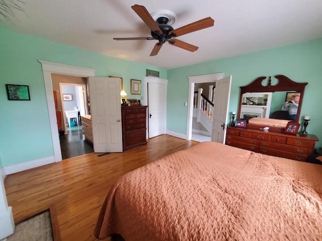 bedroom with a ceiling fan, visible vents, baseboards, and wood finished floors