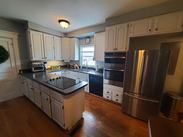 kitchen with dark wood-type flooring, a sink, white cabinetry, black appliances, and dark countertops