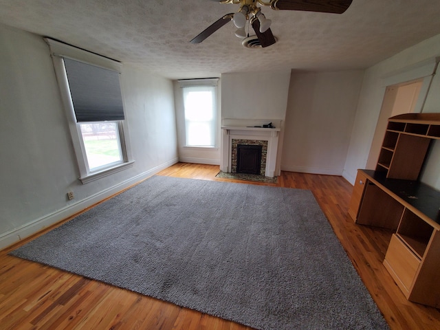 unfurnished living room featuring a textured ceiling, a fireplace with flush hearth, wood finished floors, and baseboards