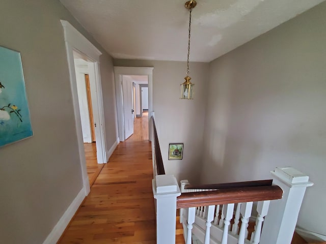 corridor with light wood finished floors, an upstairs landing, and baseboards