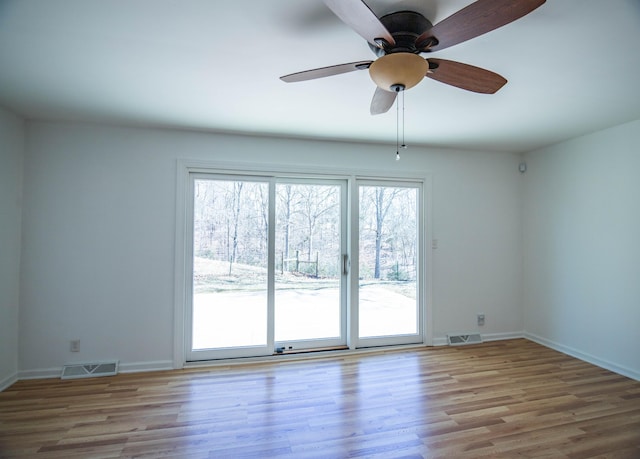 empty room featuring a ceiling fan, wood finished floors, visible vents, and baseboards