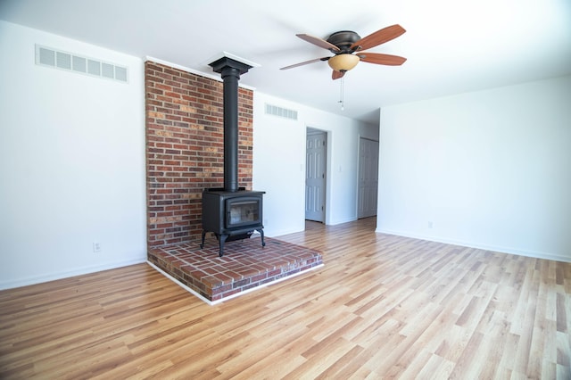 unfurnished living room with a wood stove, visible vents, and wood finished floors