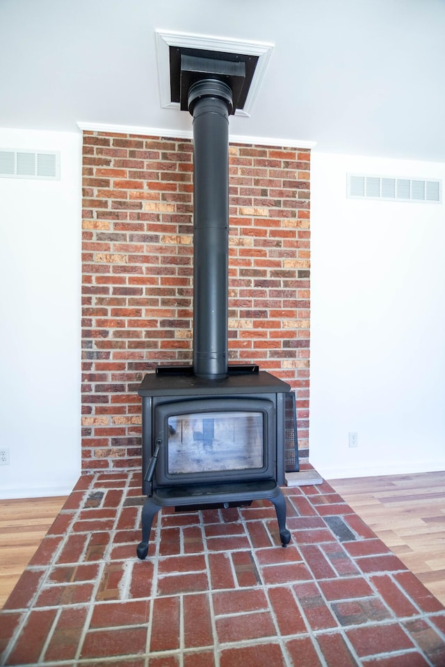 details with a wood stove, wood finished floors, and visible vents