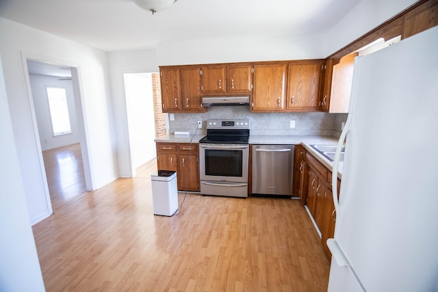 kitchen with appliances with stainless steel finishes, brown cabinetry, light countertops, and under cabinet range hood