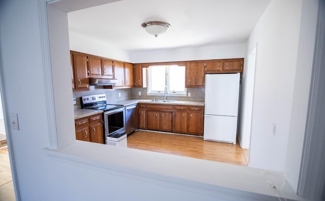 kitchen with brown cabinetry, light countertops, stainless steel appliances, under cabinet range hood, and a sink