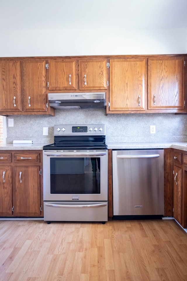 kitchen featuring light wood-type flooring, under cabinet range hood, appliances with stainless steel finishes, and brown cabinets