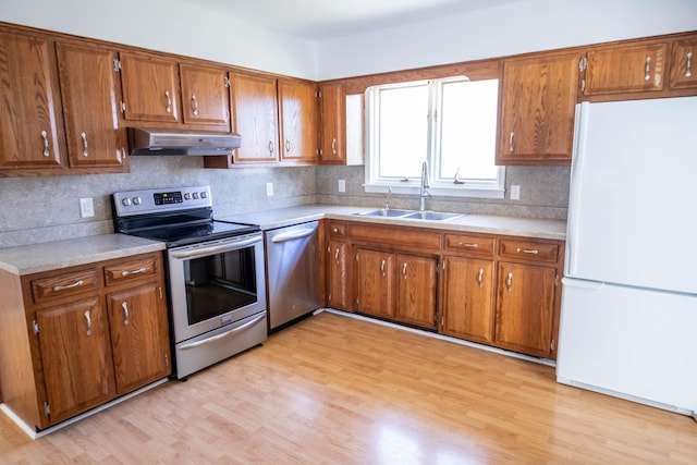 kitchen featuring under cabinet range hood, a sink, light countertops, appliances with stainless steel finishes, and brown cabinets