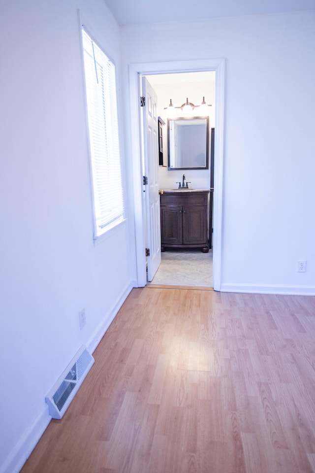 interior space with light wood-type flooring, a sink, visible vents, and baseboards