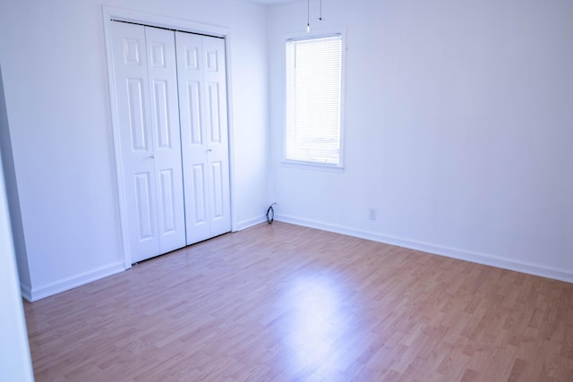 unfurnished bedroom with light wood-style flooring, baseboards, and a closet