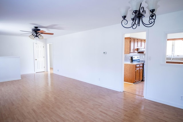 unfurnished living room with ceiling fan with notable chandelier, a sink, light wood-style flooring, and baseboards