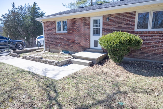 property entrance with fence, a lawn, and brick siding