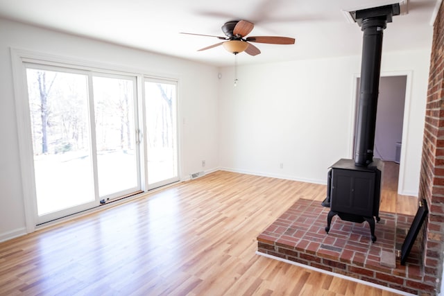 living room with baseboards, visible vents, ceiling fan, wood finished floors, and a wood stove