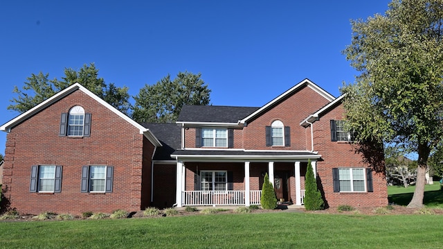 view of front of home with a front yard, covered porch, and brick siding