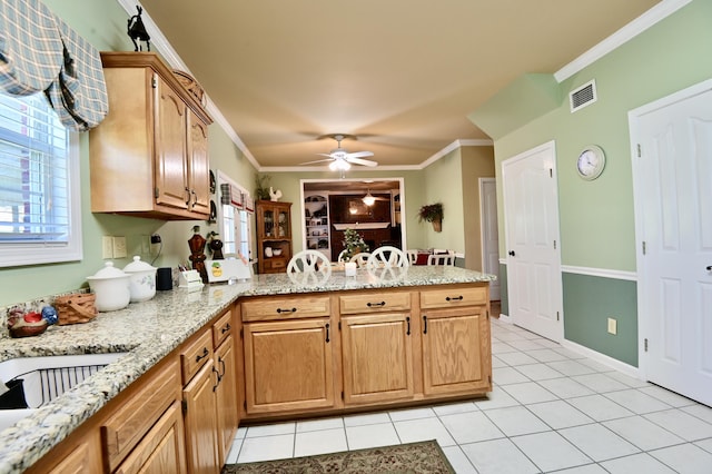 kitchen with light tile patterned flooring, a peninsula, visible vents, ornamental molding, and light stone countertops