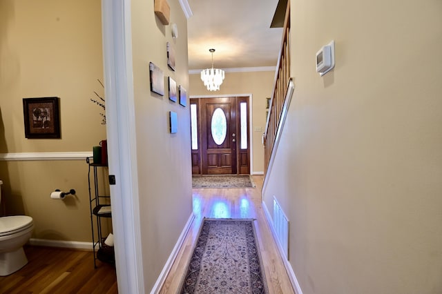 doorway to outside featuring ornamental molding, a notable chandelier, baseboards, and wood finished floors