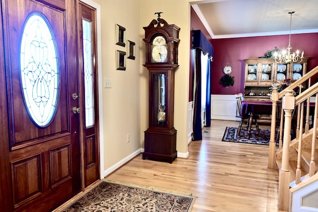 foyer entrance featuring a chandelier, light wood-style flooring, a wainscoted wall, stairs, and crown molding