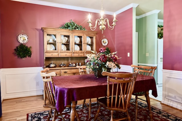 dining area featuring a wainscoted wall, light wood-style floors, a notable chandelier, and crown molding