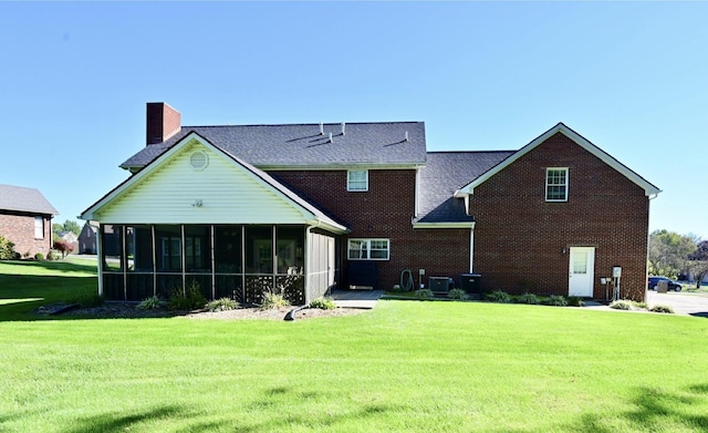 rear view of house featuring a lawn, brick siding, a chimney, and a sunroom