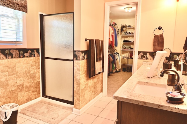 full bathroom with a wainscoted wall, a sink, a spacious closet, a shower stall, and tile patterned floors