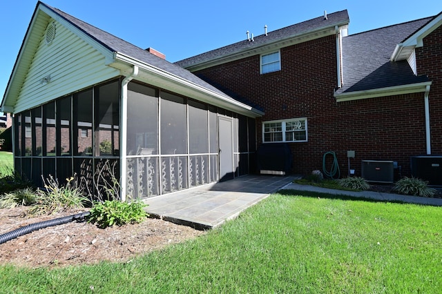 back of property featuring a sunroom, brick siding, a yard, and central AC