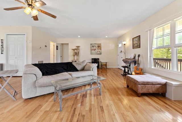 living room with light wood-type flooring, visible vents, and a ceiling fan