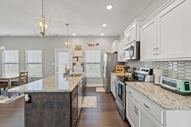 kitchen with a kitchen island with sink, a sink, appliances with stainless steel finishes, white cabinetry, and tasteful backsplash