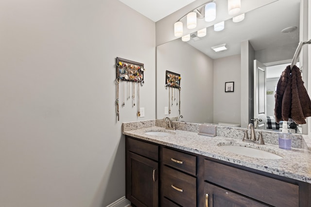 bathroom with double vanity, toilet, baseboards, and a sink