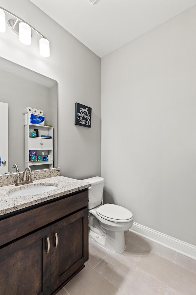 half bathroom featuring tile patterned flooring, toilet, vanity, and baseboards