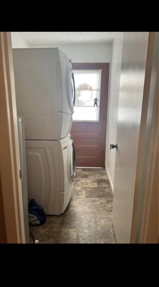 laundry area featuring laundry area, stone finish flooring, and stacked washer and dryer