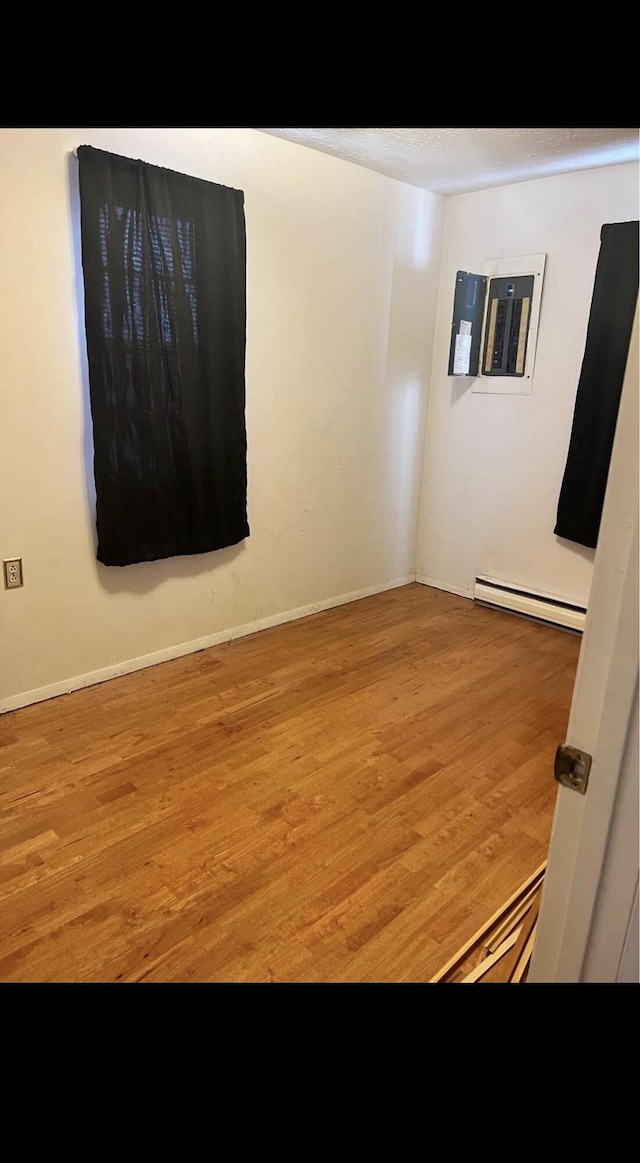 unfurnished room with electric panel, baseboards, baseboard heating, and wood finished floors