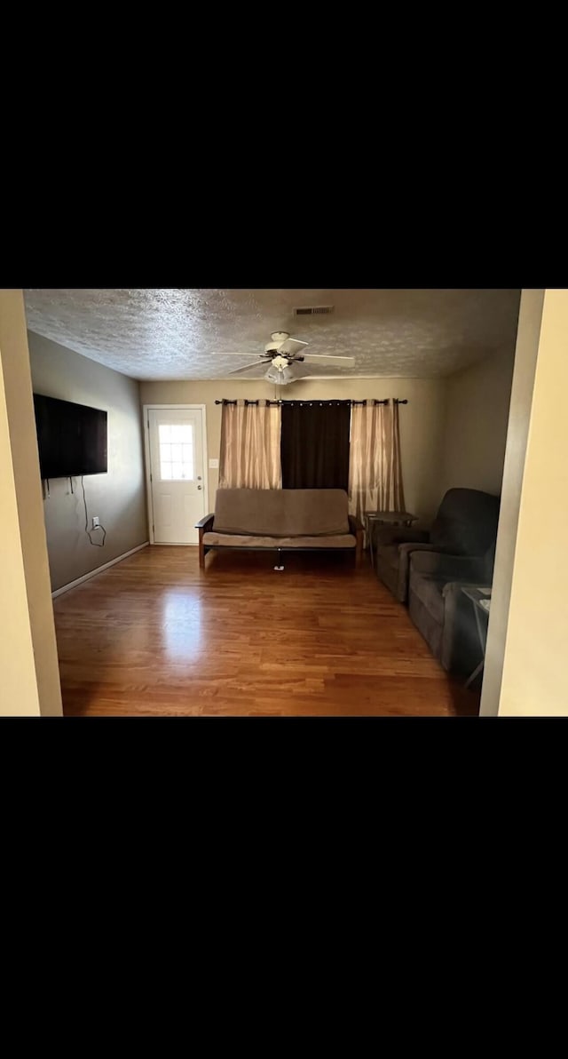 interior space featuring visible vents, ceiling fan, a textured ceiling, and wood finished floors