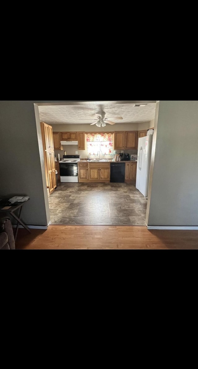 kitchen with brown cabinetry, a sink, light wood-type flooring, white appliances, and under cabinet range hood