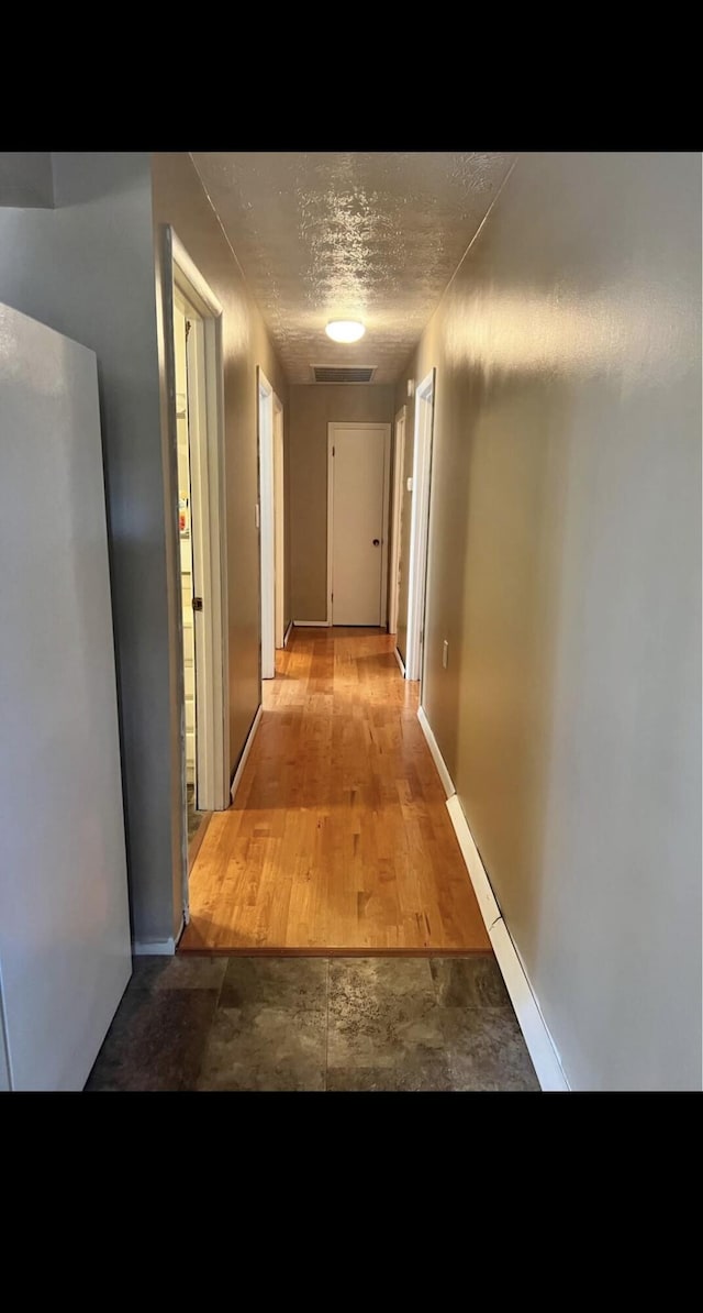 hall with visible vents, baseboards, a textured ceiling, and wood finished floors