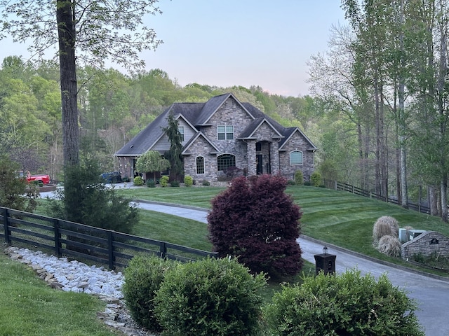 view of front facade featuring a forest view, stone siding, fence, and a front yard