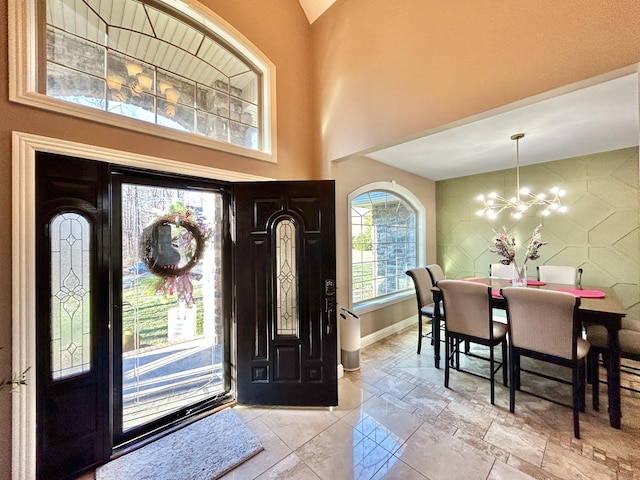 foyer with a towering ceiling, an inviting chandelier, an accent wall, and baseboards