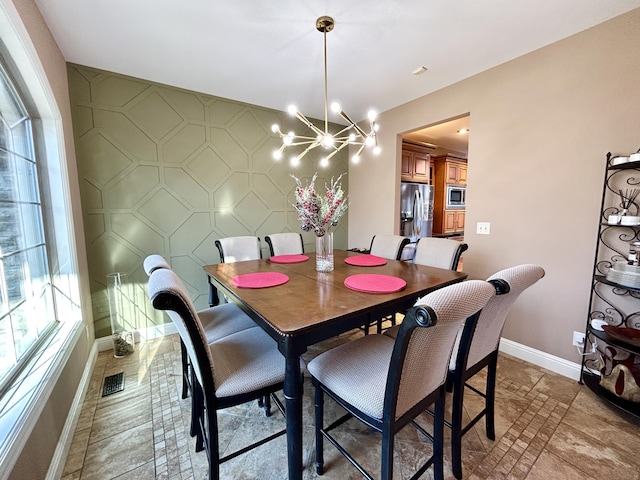 dining area featuring baseboards, visible vents, an accent wall, stone finish floor, and a chandelier